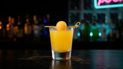 Melon Ball shot in a shot glass with bright orange-green colour from Midori, vodka and orange juice