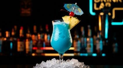 Blue Hawaiian cocktail in a hurricane glass with electric blue rum, blue curacao, pineapple and coconut cream, pineapple wedge garnish